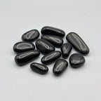 A group of smooth, polished black high gloss small pebbles arranged on a plain light gray background.