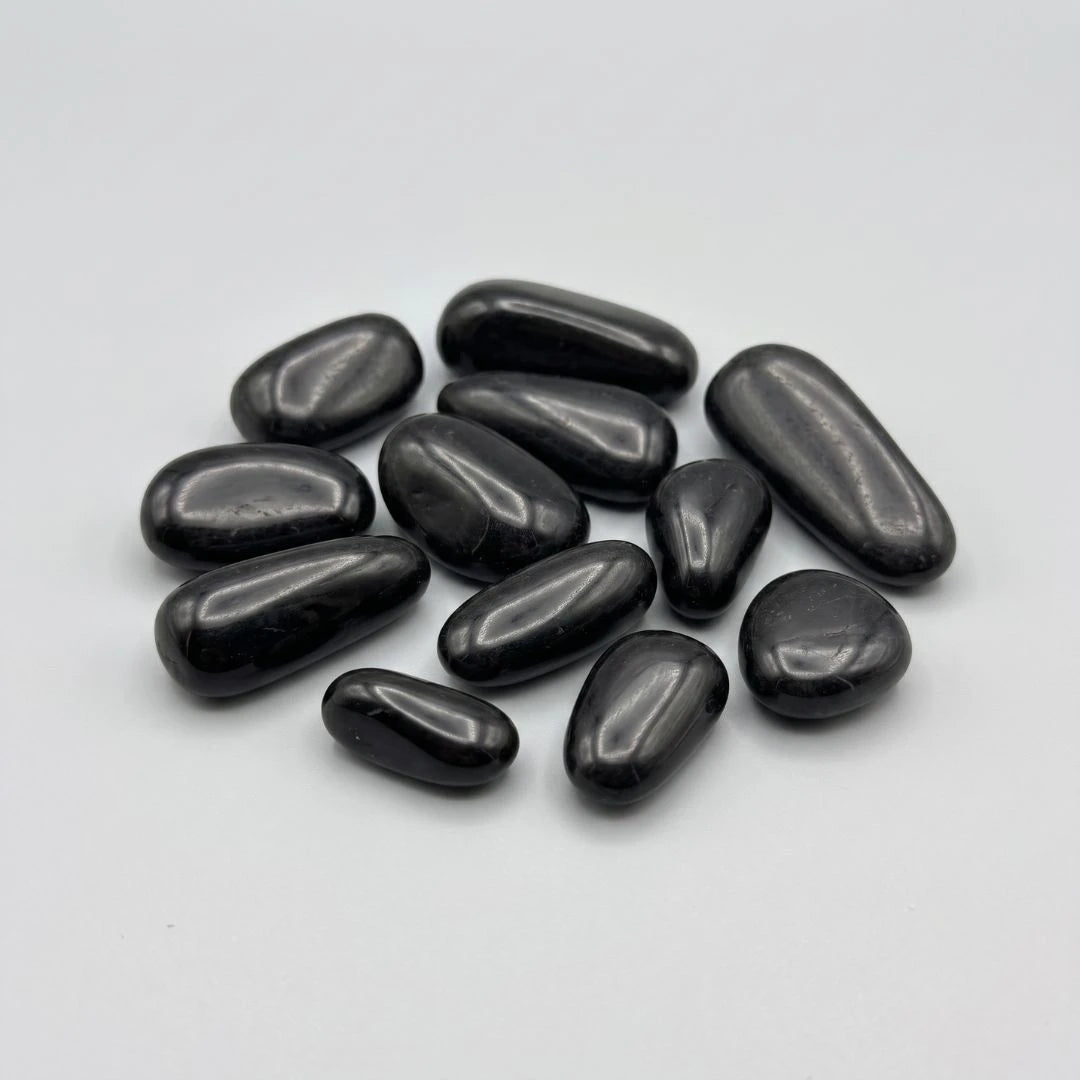 A group of smooth, polished black high gloss small pebbles arranged on a plain light gray background.