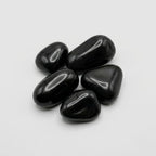 Five smooth, high gloss polished black pebbles arranged in a small cluster on a light gray background.