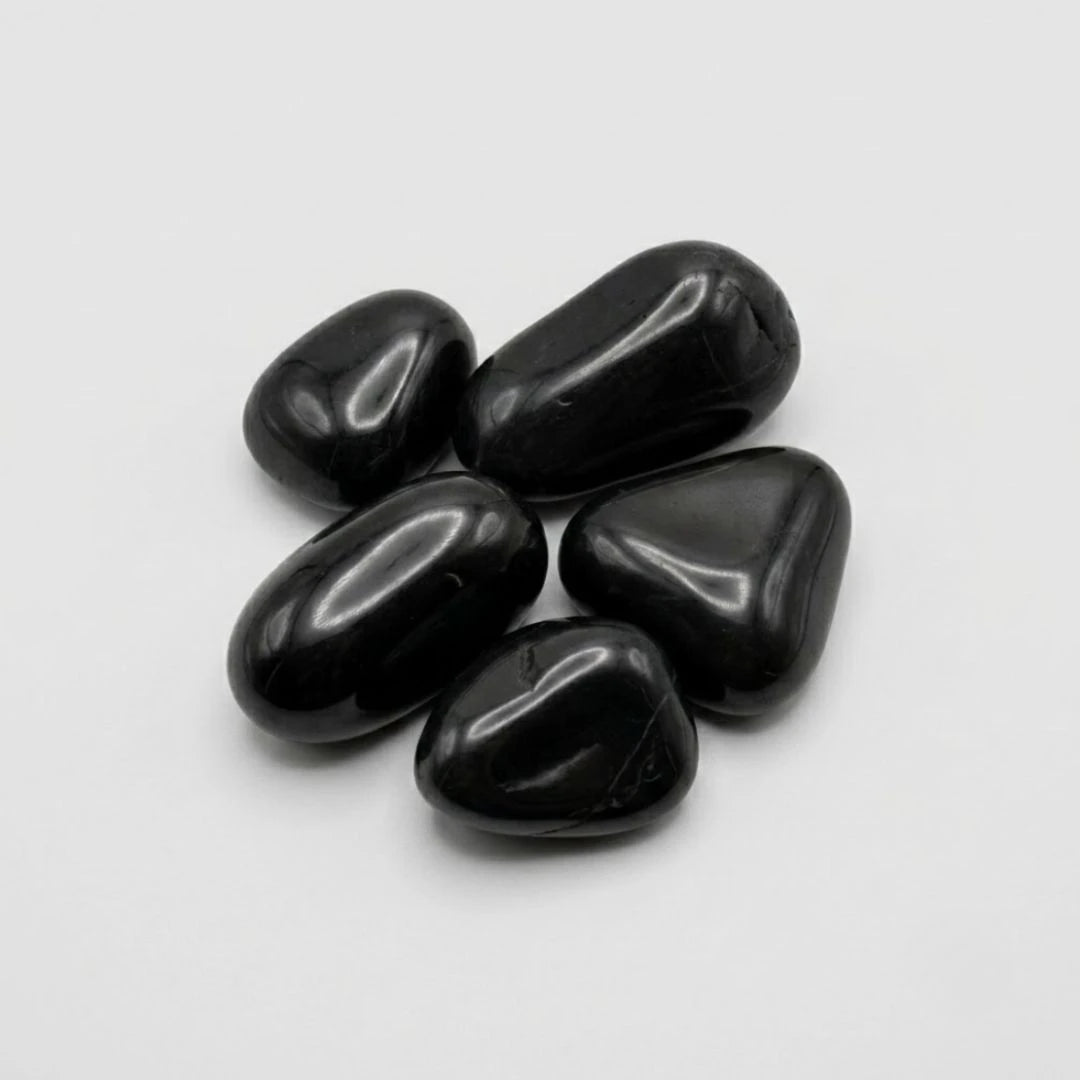 Five smooth, high gloss polished black pebbles arranged in a small cluster on a light gray background.
