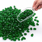 Hand holding a scoop of glossy green glass stones on a white background.