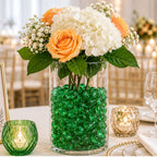 Vase with orange roses, white hydrangeas, green glass pebbles centerpiece on elegant wedding table.