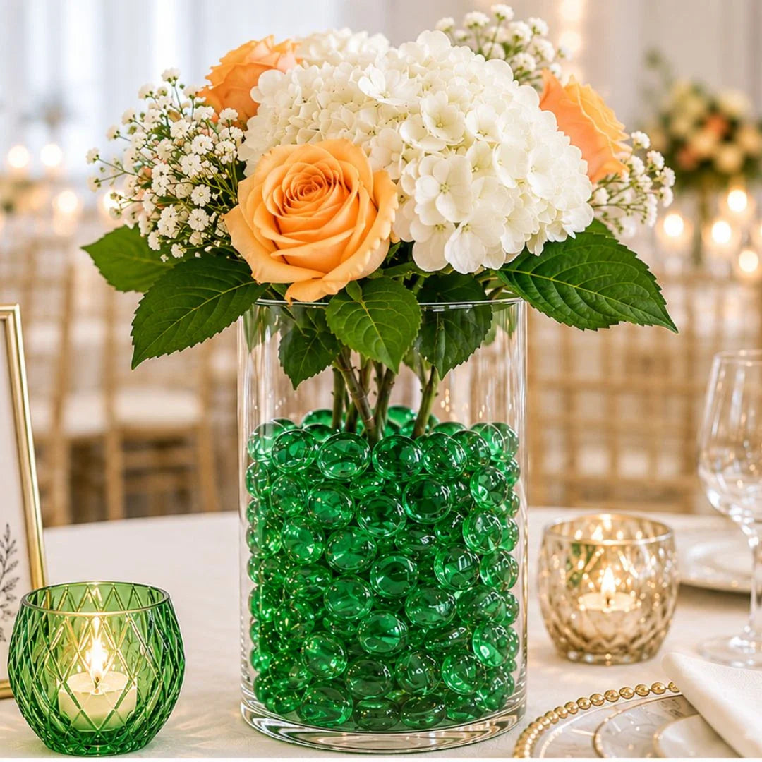 Vase with orange roses, white hydrangeas, green glass pebbles centerpiece on elegant wedding table.
