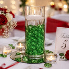 Vase with green glass stones and floating candle on wedding table, surrounded by roses and tealights.