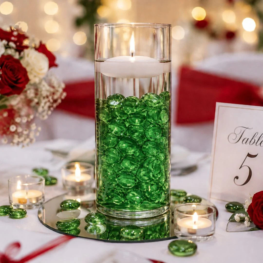 Vase with green glass stones and floating candle on wedding table, surrounded by roses and tealights.