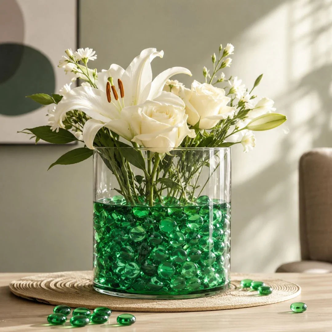 Clear vase with white flowers and green glass stones on a woven mat, sunlight streaming in.