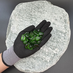 Gloved hand holding green glass pebbles on a textured gray stone background.
