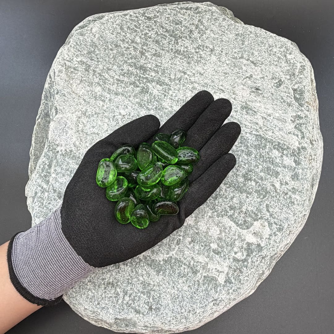 Gloved hand holding green glass pebbles on a textured gray stone background.
