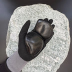 Gloved hand holding two large high-gloss polished black pebbles on a large textured stone background.