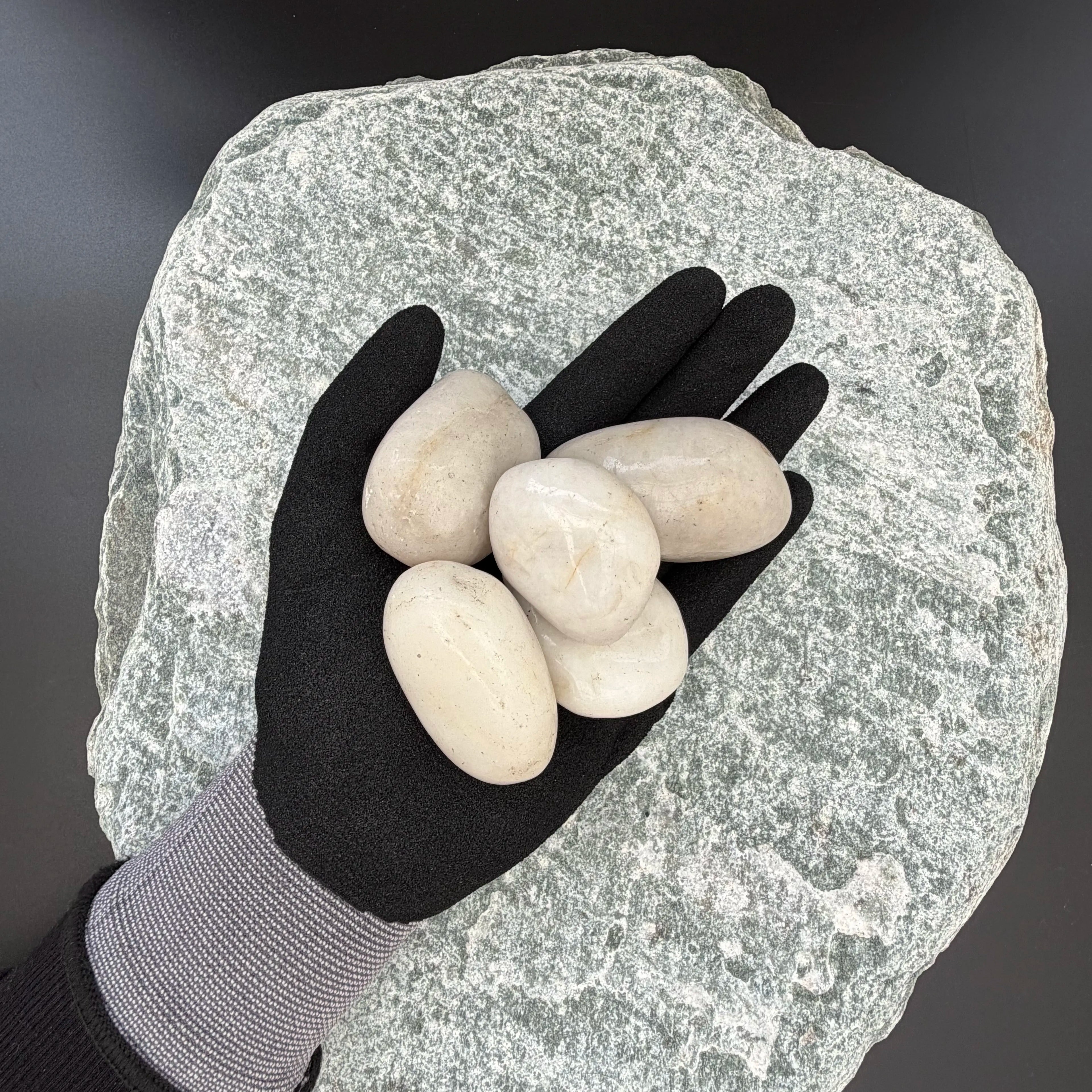 Gloved hand holding four smooth white pebbles on a textured stone background.