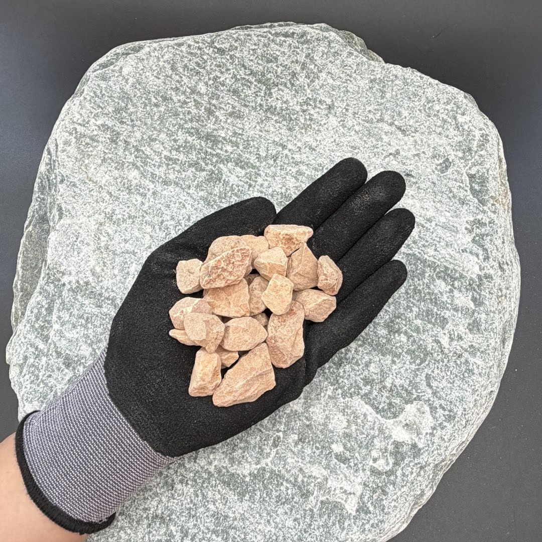 Black-gloved hand holding Italian Rosso Verona gravel pieces, 16-22mm, on a textured stone background.