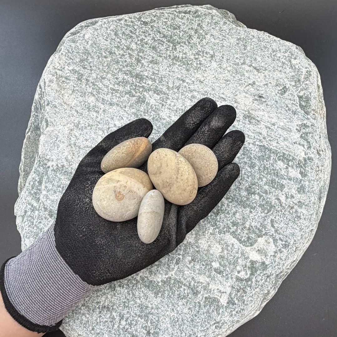 Gloved hand holding smooth multicolored pebbles on a large textured stone background.
