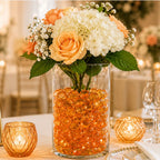 Vase with orange glass stones and peach roses, white hydrangeas, and baby's breath centerpiece on a decorated table.