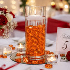 Vase with orange glass stones and floating candle on wedding table with red roses and table number 5.