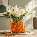 Clear vase with white flowers and orange glass stones on a woven placemat.