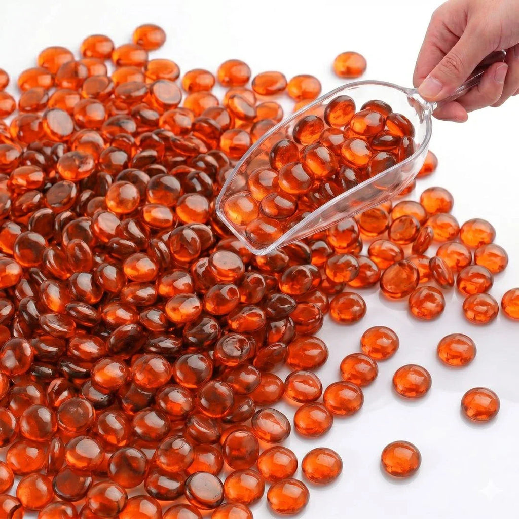 Hand scooping orange glass pebbles onto a white surface.