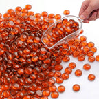 Hand scooping orange glass pebbles onto a white surface.