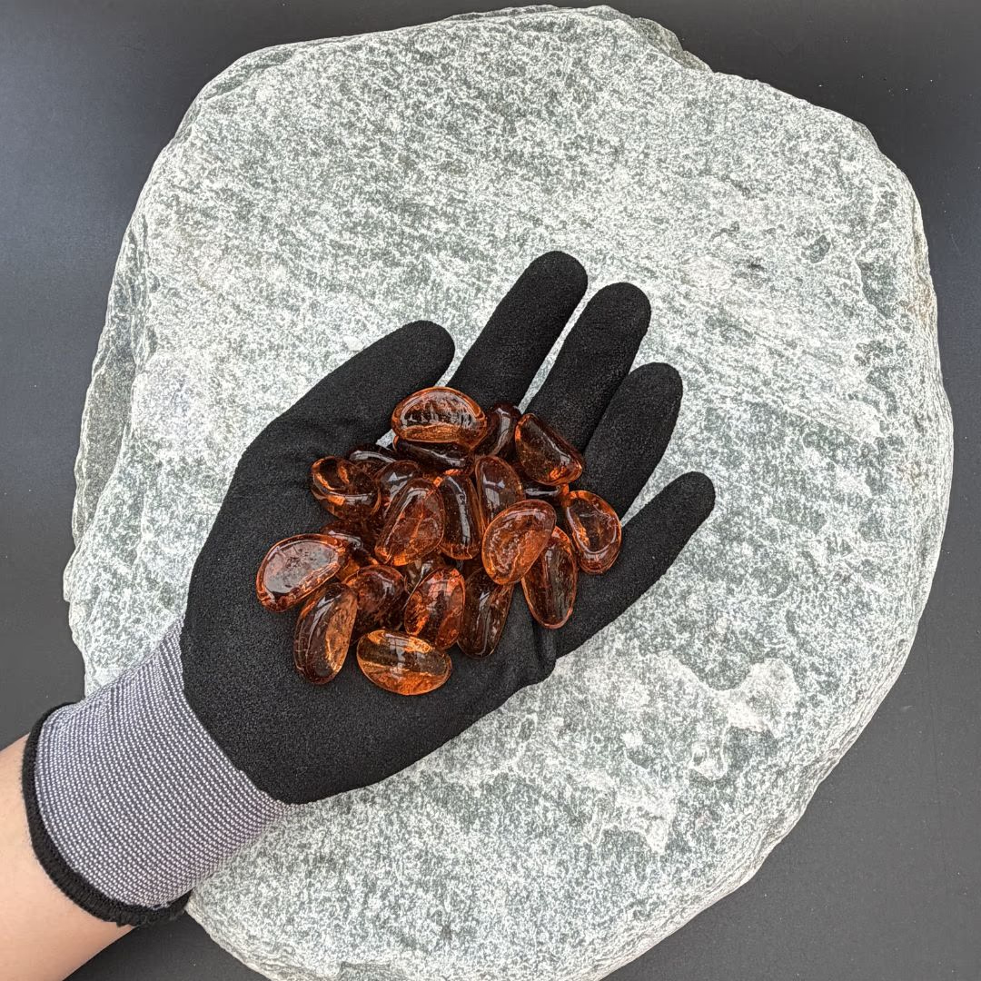 Gloved hand holding orange glass pebbles on a large grey stone background.