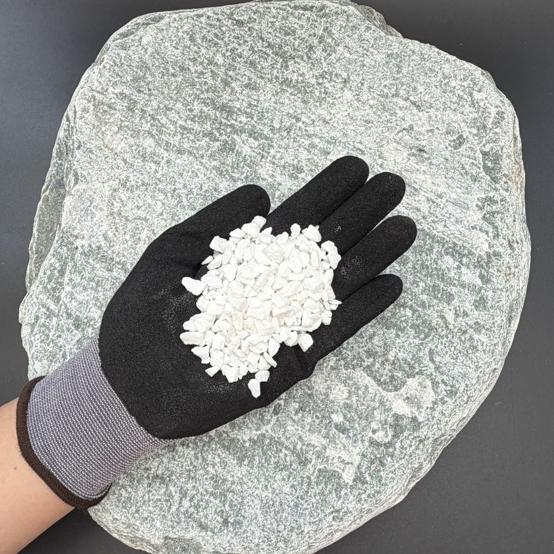 Gloved hand holding small white gravel pieces over a large flat stone surface.
