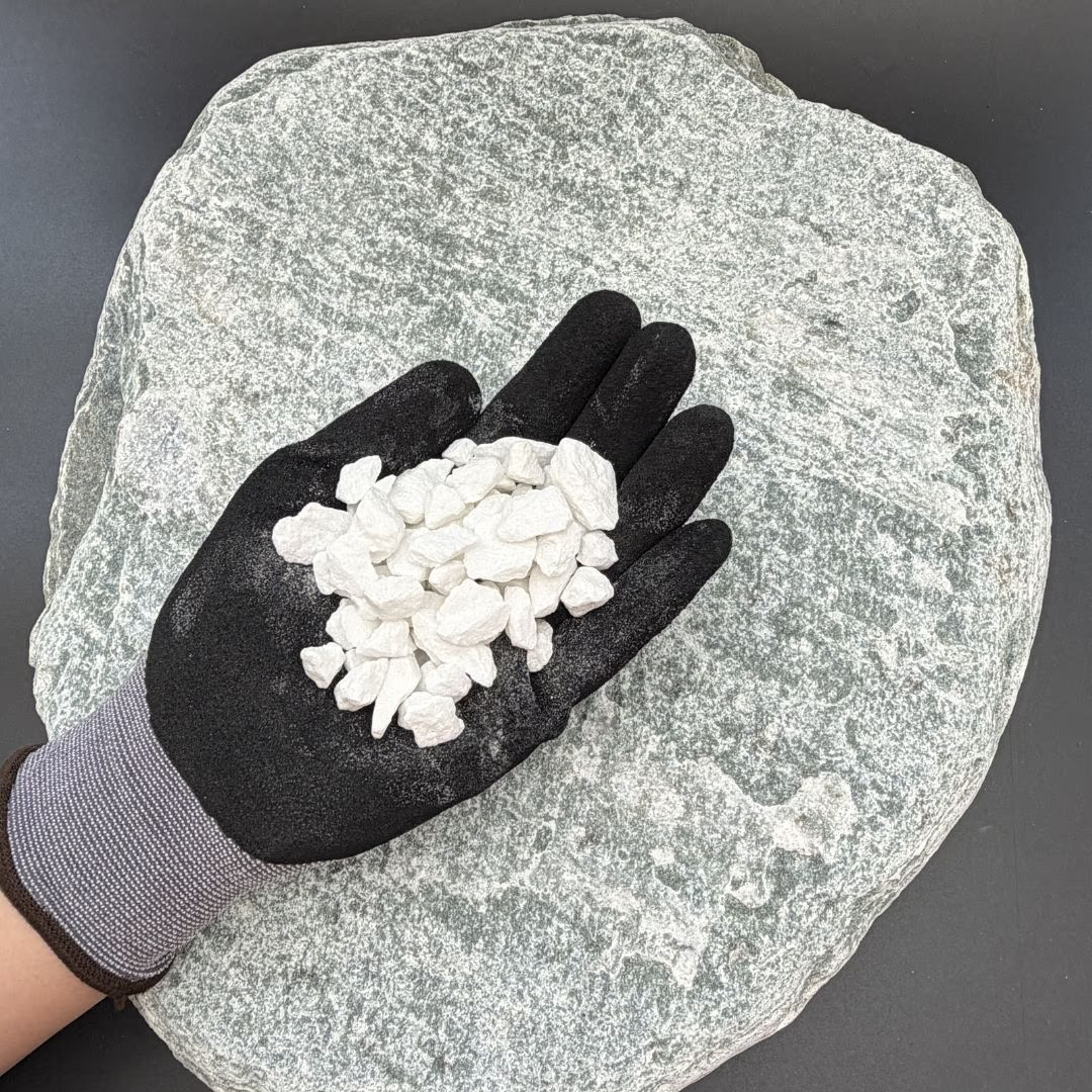 Gloved hand holding white gravel atop a large, textured stone surface.