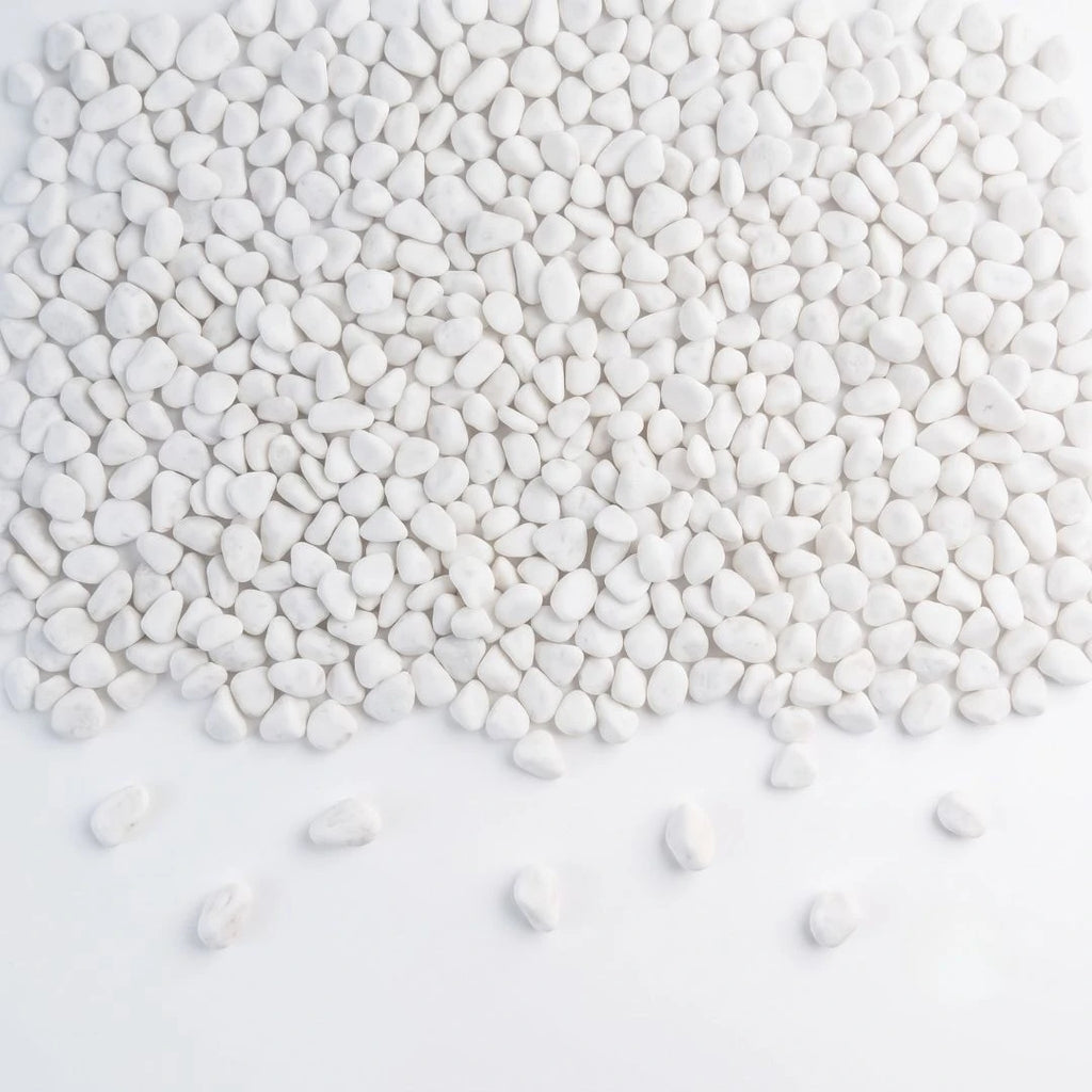 White decorative pebbles scattered across a white background, with a few stones lying on the surface in front of the pile.