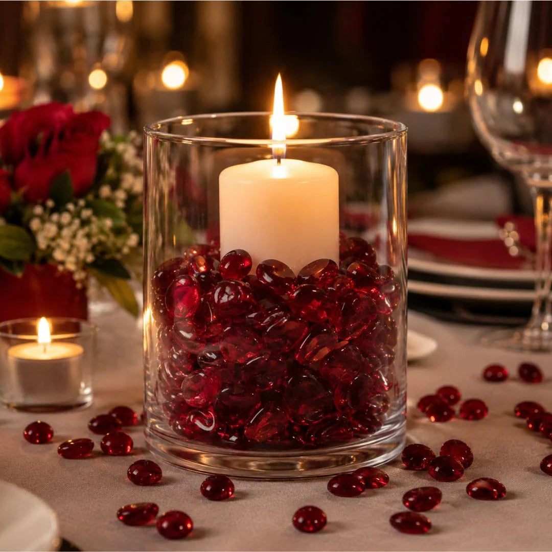 Vase with red glass stones and lit candle on a decorated table with roses and tableware.