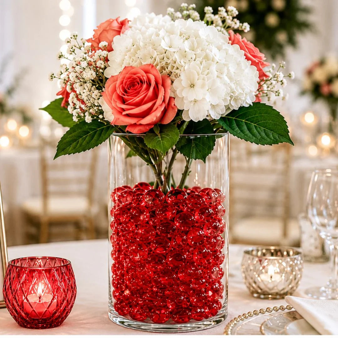 Vase with red glass stones and floral arrangement on an elegant table setting with candles.