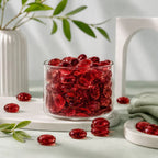 Clear vase filled with red glass stones on a table with scattered stones, a white vase, and greenery.
