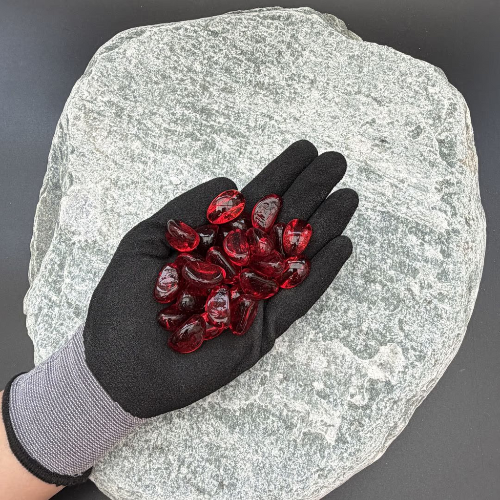 Gloved hand holding red glass pebbles on a textured stone background.