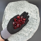 Gloved hand holding red glass pebbles on a textured stone background.