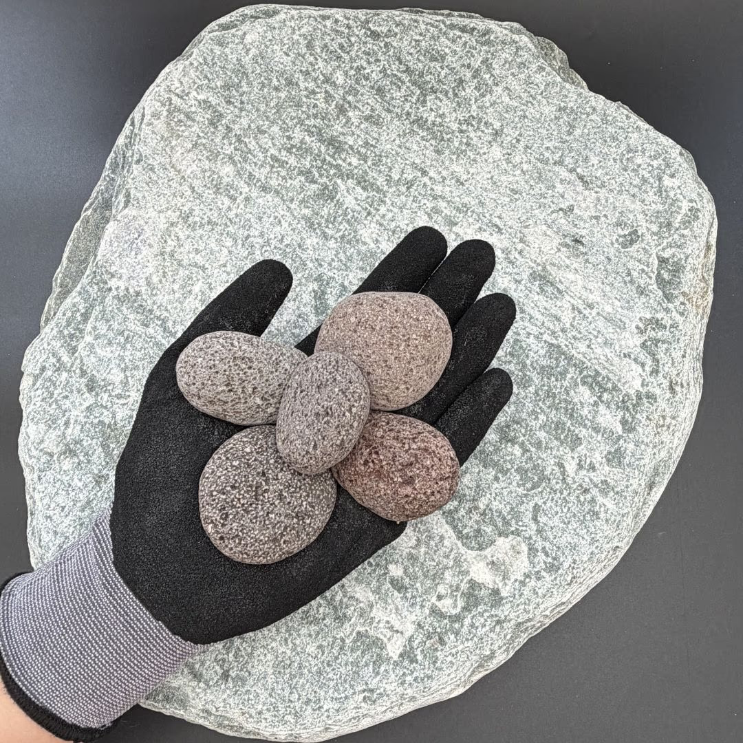 Gloved hand holding five red lava stones on a large grey stone background.